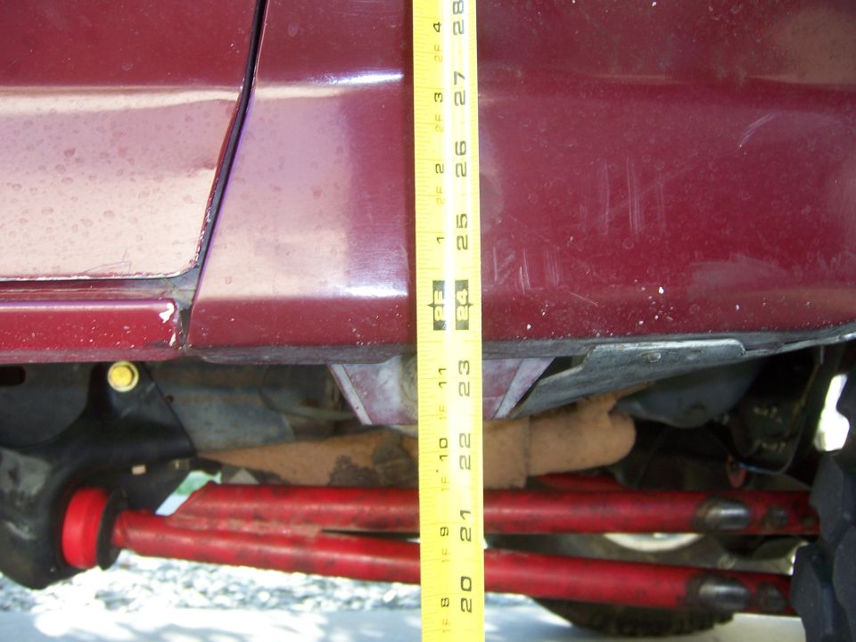 Yellow measuring tape against red vehicle body, showing suspension components below