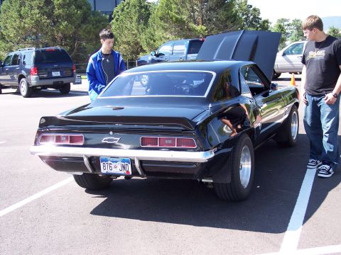 1972 Ford Ranchero - A black 1969 Chevrolet Camaro is parked with its hood up, viewed from the rear, with two people standing nearby.
