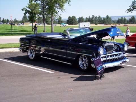 1972 Ford Ranchero - A dark blue convertible is displayed with its hood open, revealing the engine bay. A sign identifies it as a 1953 Chevy Bel Air.
