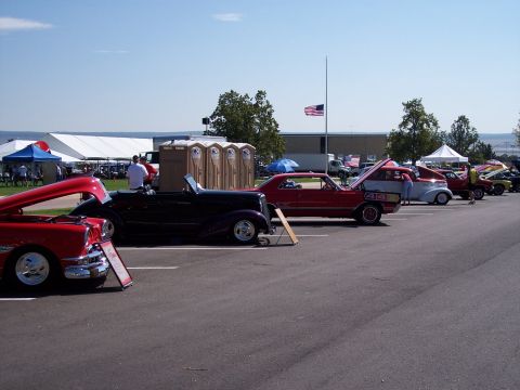 1972 Ford Ranchero - A red car with its hood open is parked at a car show, with other vehicles and tents in the background.
