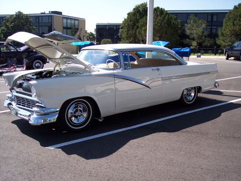 1972 Ford Ranchero - White 1956 Ford Fairlane Crown Victoria, hood up, parked in a lot with other vehicles.