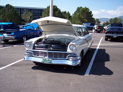 1972 Ford Ranchero - A white 1955 Ford Fairlane is displayed with its hood open, parked in a lot alongside other vehicles.