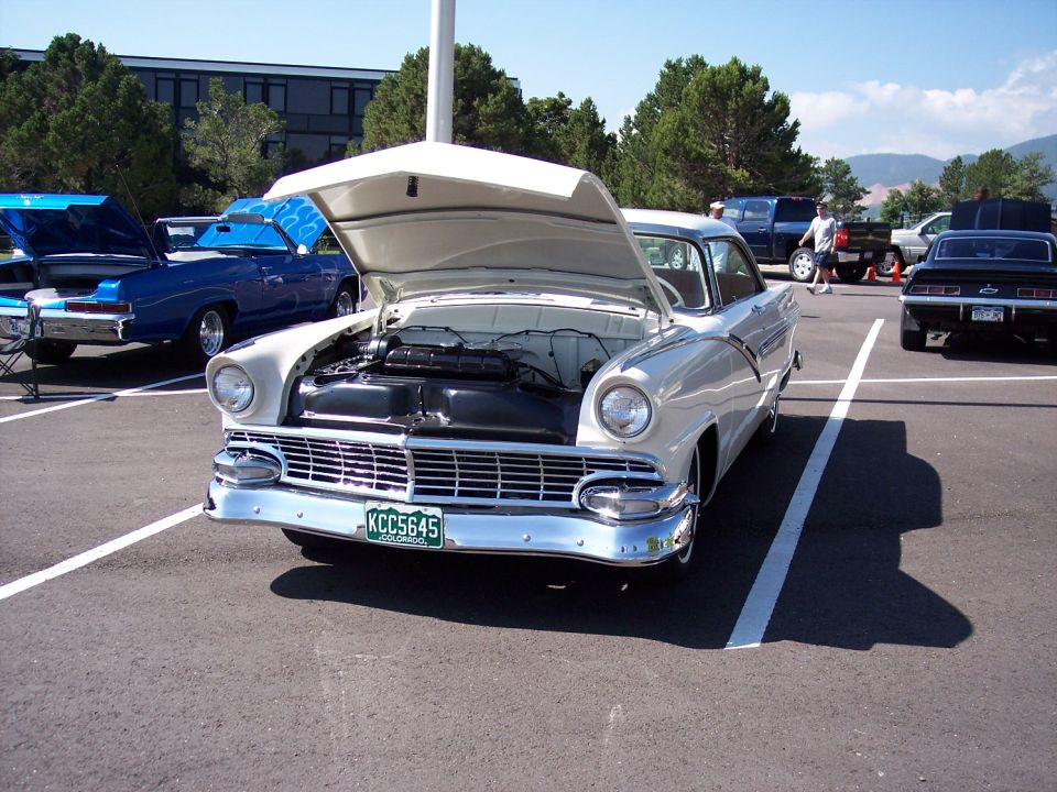 White 1950s Ford Fairlane with hood open, parked in a lot. License plate reads KCC5645
