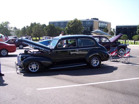 1972 Ford Ranchero - A classic black sedan is displayed with its hood open, custom chrome wheels at a car show.