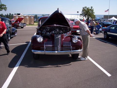 1972 Ford Ranchero - A man examines a vintage maroon car with its hood raised at an outdoor car show.