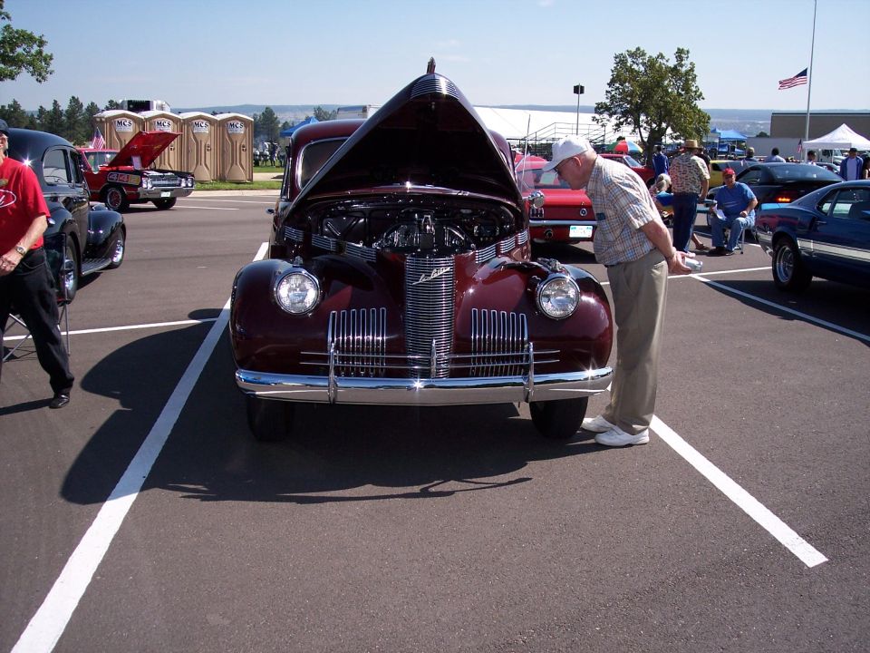 Maroon vintage car with hood open, viewed from the front. Chrome grille and bumper are visible