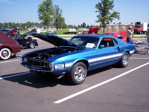 1972 Ford Ranchero - A blue muscle car with white racing stripes is parked with its hood open at an outdoor event.