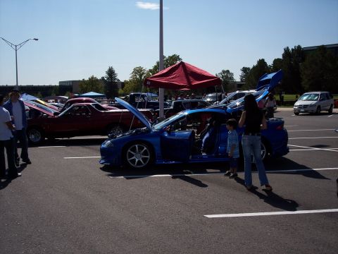 1972 Ford Ranchero - A car show features several vehicles, including a blue sports car with its doors open and a red pickup truck.