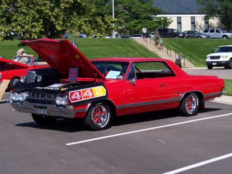 1972 Ford Ranchero - A bright red 1964 Oldsmobile 442 is displayed with its hood open, revealing the engine and a prominent 442 decal on the black inner hood pa…