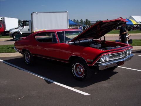 1972 Ford Ranchero - A red muscle car with its hood open is parked on asphalt, with a white truck in the background.