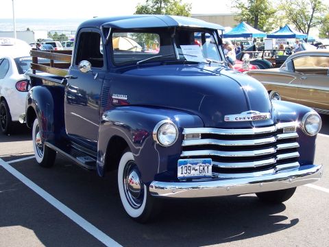 1972 Ford Ranchero - A classic blue Chevrolet pickup truck is displayed at an outdoor car show with other vehicles in the background.