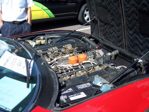 1972 Ford Ranchero - The engine bay of a red car is visible, dual carburetors and orange air filters. A sign is placed on the windshield.