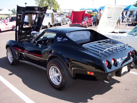1972 Ford Ranchero - A black Corvette with its hood open is displayed at an outdoor car show, with other vehicles and tents visible.