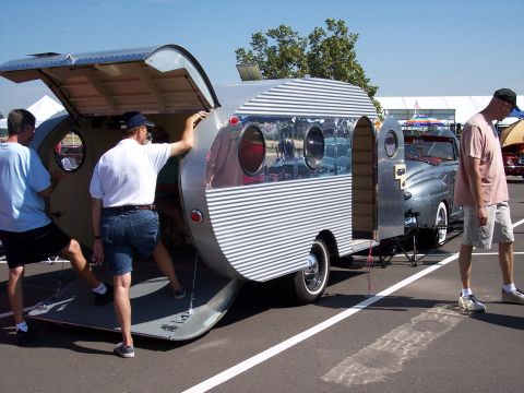 1972 Ford Ranchero - A vintage silver teardrop trailer is open for viewing, parked next to a classic grey convertible.