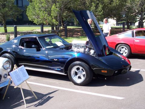 1972 Ford Ranchero - A black 1975 Chevrolet Corvette with custom blue flame paint and an exposed engine is displayed at an outdoor event next to a red car.