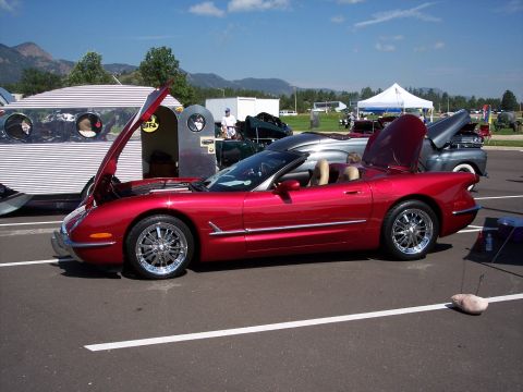 1972 Ford Ranchero - A red convertible sports car is parked with its hood open next to a vintage trailer.
