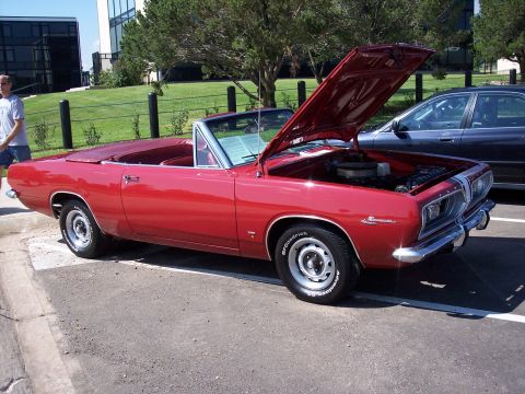 1972 Ford Ranchero - A red convertible is parked outside a modern building with its hood open, revealing the engine bay.