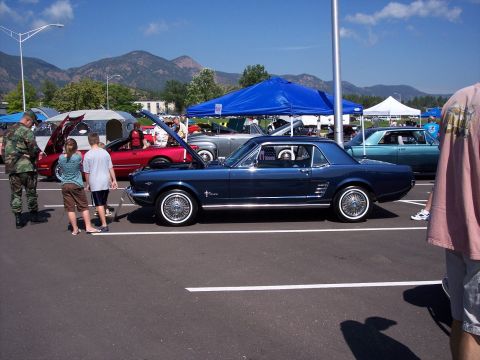 1972 Ford Ranchero - A dark blue 1965 Ford Mustang coupe is displayed with its hood open at an outdoor car show.