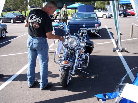 1972 Ford Ranchero - A man cleans a motorcycle at an outdoor car show with other vehicles in the background.