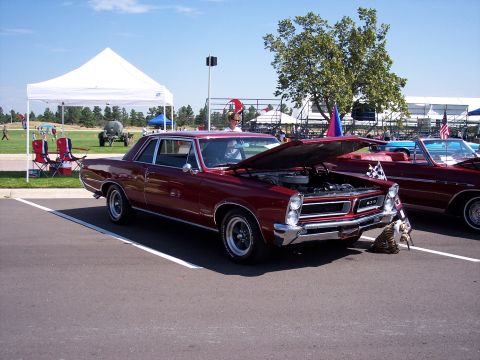1972 Ford Ranchero - A red 1965 Pontiac Tempest GTO is displayed with its hood open, parked beside another vehicle at an outdoor event.