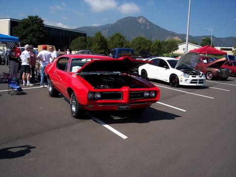 1972 Ford Ranchero - A classic red Pontiac GTO is displayed at a car show, with other vehicles and spectators present under a clear sky.