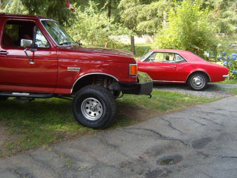 1989 Ford Bronco - A red 1989 Ford Bronco is parked next to a classic red coupe in a grassy area.