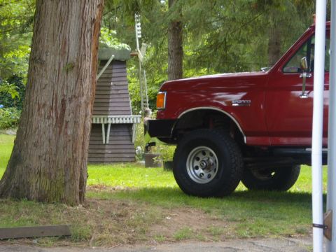 1989 Ford Bronco - A red 1989 Ford Bronco is parked on a grassy lawn near a tree and a decorative windmill.