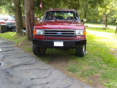 1989 Ford Bronco - A red Ford truck is parked outdoors with a black aftermarket bumper and a "4x4" badge visible.