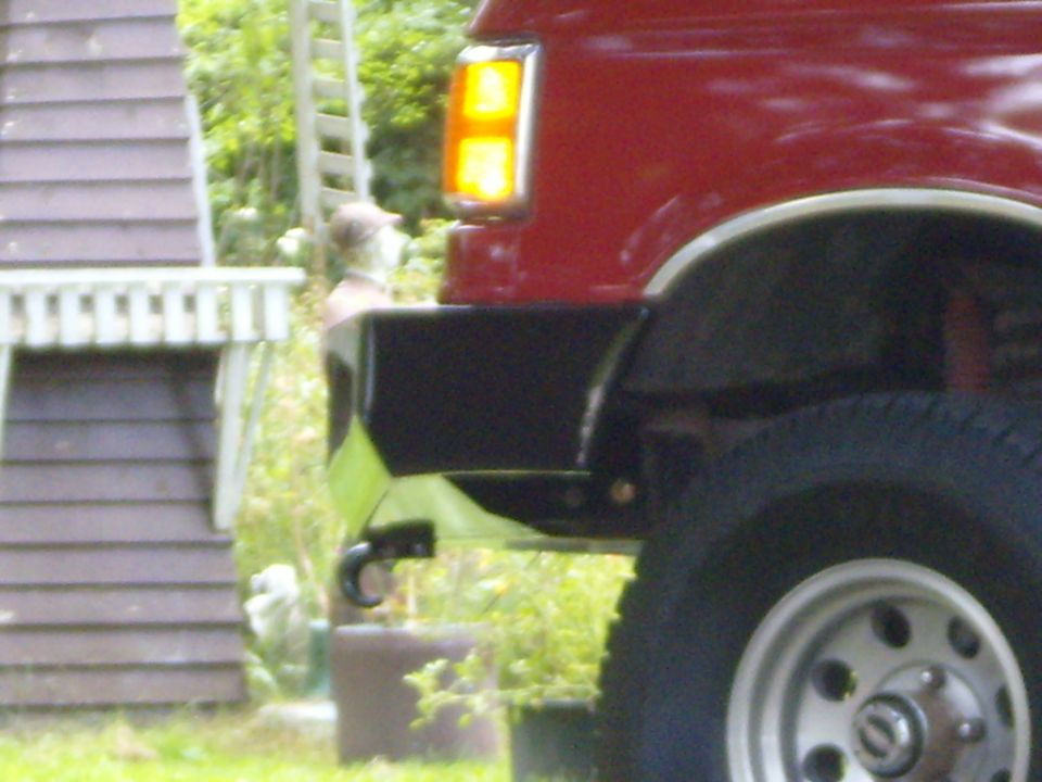 Red SUV's rear corner with a black bumper and tow hook. A ladder is visible in the background