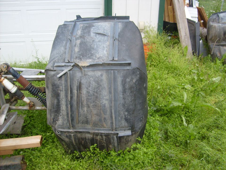 Black plastic fuel tank with metal straps, resting in grass near a garage door