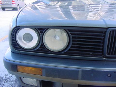 1989 BMW 3 Series - Close-up of the front grille and headlights of a car, with another vehicle in the background.