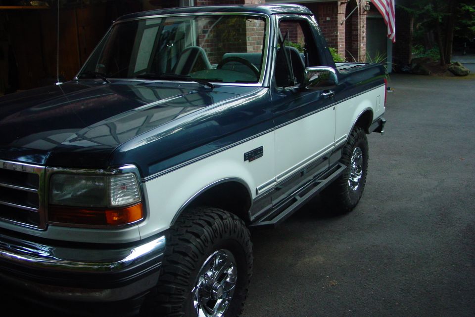 Dark blue and white Ford Bronco with running boards and chrome wheels