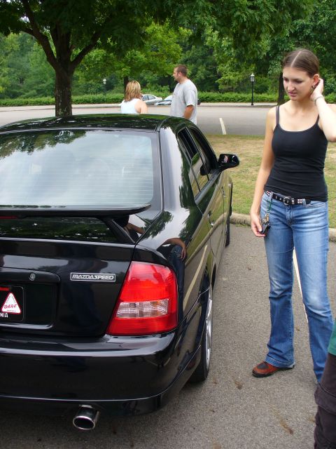 1991 Ford Probe - A black MazdaSpeed sedan is parked in a lot, with a woman standing nearby.