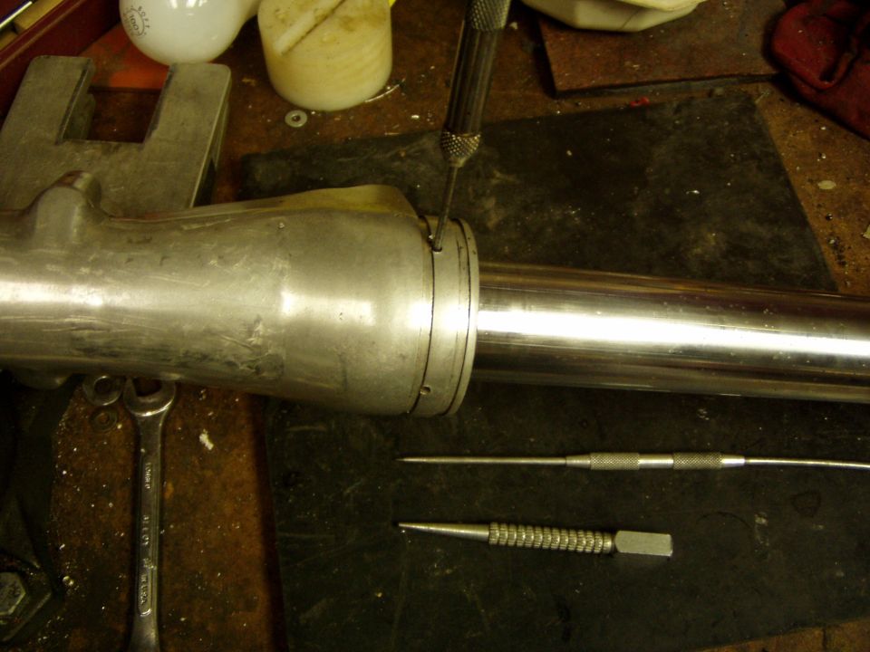 Fork lower leg and chrome tube on a workbench with a punch on the seal retaining ring and tools nearby