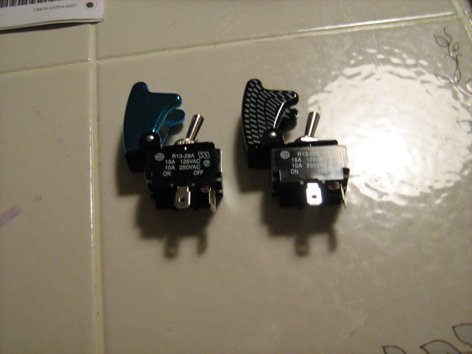 Two toggle switches, one with a teal cover and one with a carbon fiber pattern cover