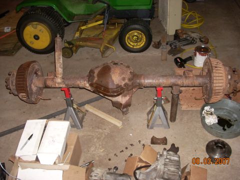 2000 Chevrolet Tahoe - A heavily rusted rear axle assembly is supported by jack stands in a garage setting.