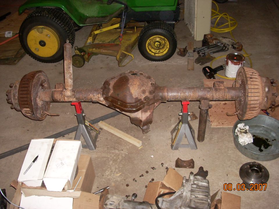 Rusty rear axle assembly on jack stands, with a lawn tractor in the background