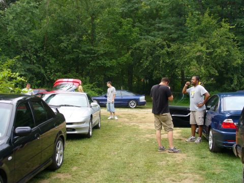 1991 Ford Probe - Several cars and people are gathered outdoors in a grassy area with trees in the background.