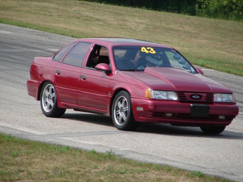 1993 Ford Taurus - A red sedan, possibly a 1992 model, navigates a turn on a road course with racing modifications.