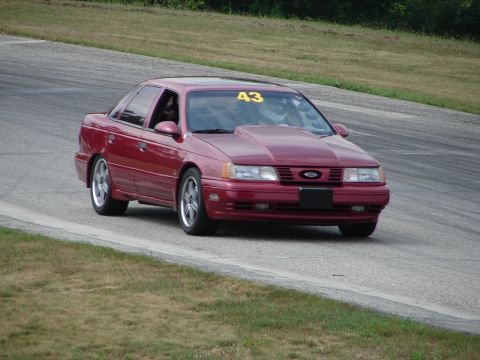 1993 Ford Taurus - A red 1993 Ford Taurus with racing number 43 on the windshield navigates a turn on a road course.