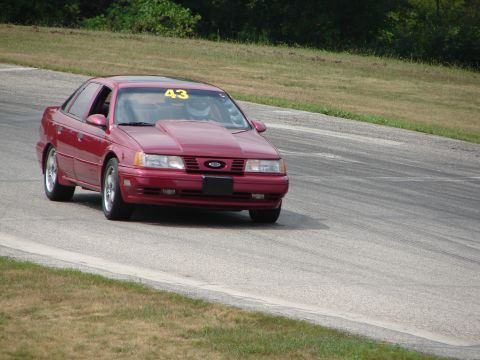 1993 Ford Taurus - Red 1993 Ford Taurus with a hood scoop and racing number 43 drives on a track.