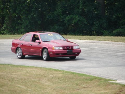 1993 Ford Taurus - A red sedan with a modified hood scoop navigates a turn on a race track.