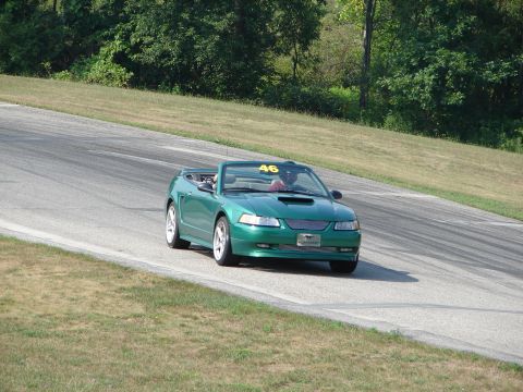 1993 Ford Taurus - A green convertible sports car, likely a Ford Mustang from the early 2000s, navigates a turn on a race track.