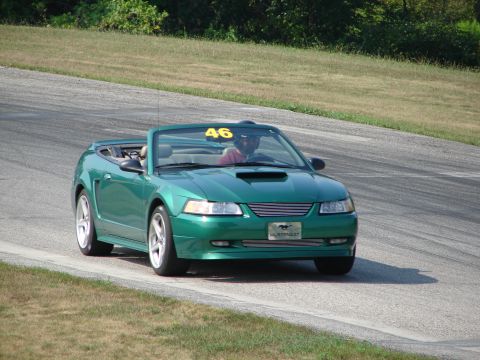 1993 Ford Taurus - Green convertible Mustang with racing number 46 navigates a turn on a road course.