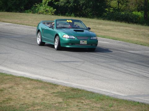 1993 Ford Taurus - A green convertible sports car with a racing number is driving on a paved track with grassy areas on the sides.