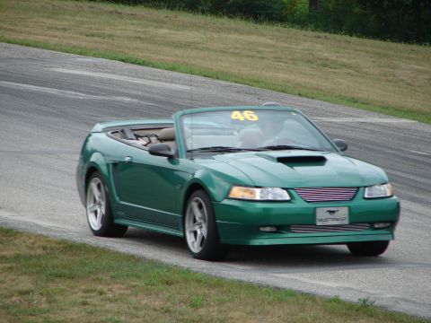 1993 Ford Taurus - A green convertible Mustang with racing number 46 visible on the windshield drives on a road course.