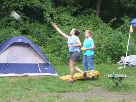 1991 Ford Probe - People enjoy a game of cornhole outdoors near a tent, with a small table and drink visible.