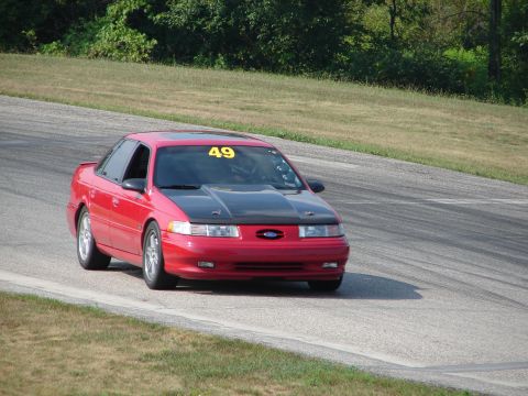 1993 Ford Taurus - Red 1993 Ford Taurus with racing number 49 navigates a turn on a road course.