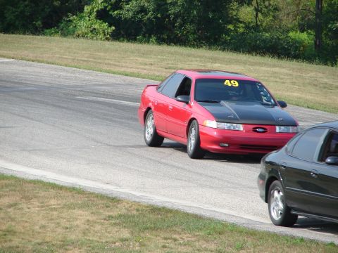 1993 Ford Taurus - A red sedan, identified as a 1993 Ford Taurus, navigates a road course with racing number 49 displayed.