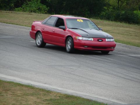 1993 Ford Taurus - A red 1993 Ford Taurus with a black hood and racing number 49 navigates a turn on a road course.